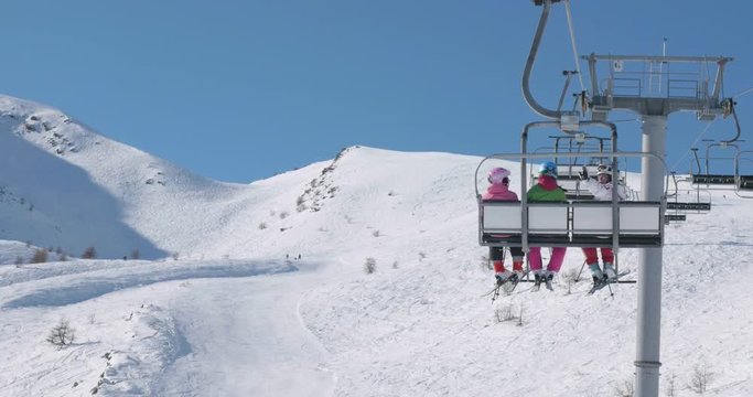 Shot from behind, how teen girls rides a ski lift and have a good time
