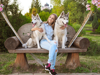 Attractive young woman sits on a bench with two funny siberian husky dogs