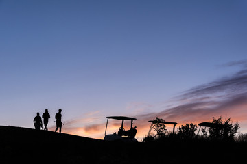 golfers and golf carts silhouetted by sunset