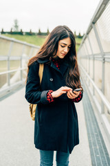 Knee figure of young beautiful long hair model woman outdooe in the city in winter using smart phone hand hold - technology, texting, social network concept