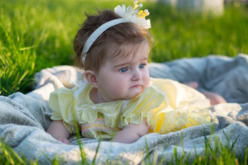 A little girl (six months old) with a crown on her head is lying on the lawn.  She's upset and going to cry.