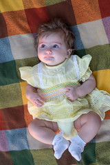 Little girl (six months old) in yellow dress is lying on a plaid