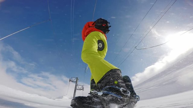 Snowboarder riding a ski tow up the hill, low angle rear view
