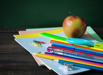 School supplies on a wooden old surface. Notebooks, handles, colored pencils  and red apple on a wooden table