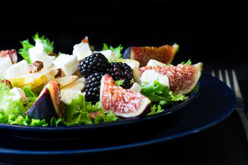 Salad with pears, lettuce, figs, walnuts, goat cheese, walnuts and honey on black background
