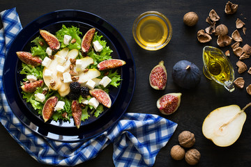 Salad with pears, lettuce, figs, walnuts, goat cheese, walnuts and honey on black background