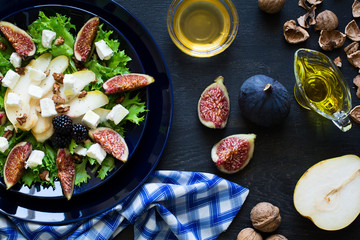 Salad with pears, lettuce, figs, walnuts, goat cheese, walnuts and honey on black background