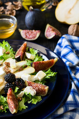 Salad with pears, lettuce, figs, walnuts, goat cheese, walnuts and honey on black background