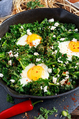 Homemade Green Kale with eggs, feta cheese, herbs in iron pan. healthy rustic breakfast