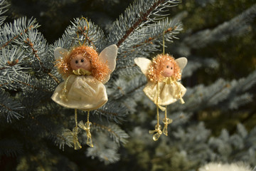 Рождественская игрушка в виде ангела. Игрушка расположена на елке. Ангел в белой одежде. Ангел имеет золотистые волосы