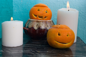 oranges with carved faces with white candles and a clay pot on a blue background with the autumn Halloween theme