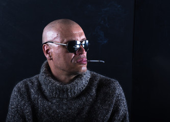 studio portrait of a bald man with glasses and a cigarette