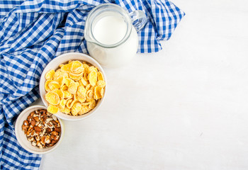 Light healthy breakfast: cornflakes, milk and nuts for them. On wooden white table, top view, copy space