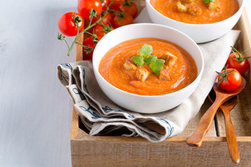 Tomato soup with cream, croutons and parsley on a white wooden table