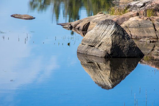 triangular rock reflecting into calm, blue lake at sunrise