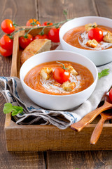 Tomato soup with cream and croutons and parsley leaves in a white bowl on a napkin on a wooden table vertical view