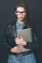 Beautiful young girl. Glasses, denim overalls, a black leather jacket. Woman with folders. Sexy girl. Trendy toning image.