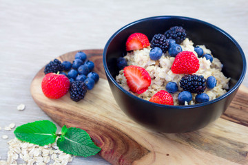 Oatmeal porridge in bowl topped with blueberries, blackberry, strawberries and mint. Healthy breakfast with vitamins