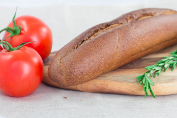 Brown bread, rosemary, tomato on cutting board. Close up bread concept.
