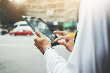 Close-up image of young professional businessman using modern digital tablet outside, urban street in the blurred background, flare light