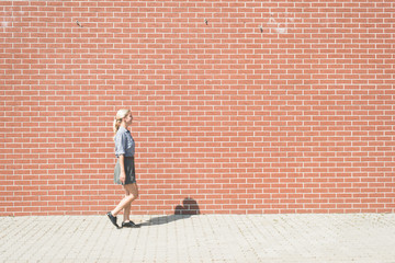 Young successful business woman walking against brick wall 