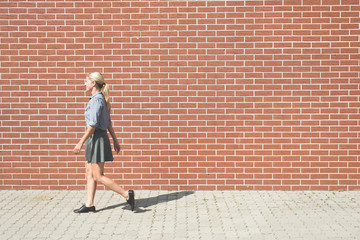 Fototapeta na wymiar Young successful business woman walking against brick wall 