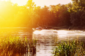 boat pulls man water skiing on the river. Sunset. Splashes of water.