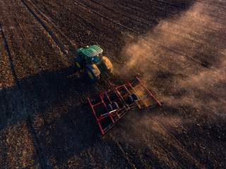 Naklejka premium Tractor cultivating field at autumn