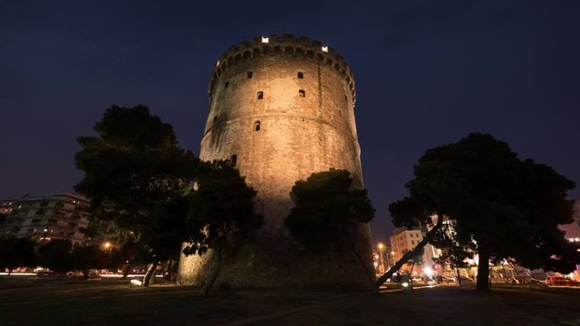 Timelapse and low angle shot of city life around the White Tower of Thessaloniki which illuminated when night coming
