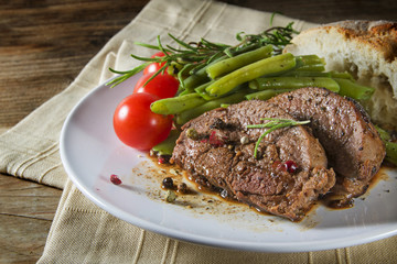 dish of grilled lamb steak with green beans, tomatoes and bread on rustic wood
