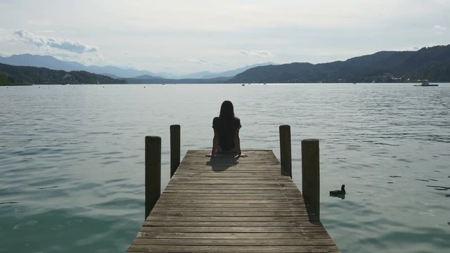 Relaxation at mountain lake. Woman sits on dock