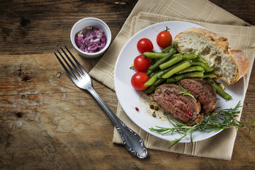 dish of grilled rosemary lamb steak with green beans and tomatoes on rustic wood from above © Maren Winter