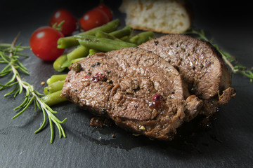 grilled lamb steak with green beans, tomatoes and rosemary on dark slate, close up