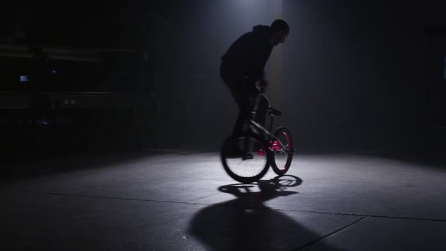BMX rider doing tricks in dark warehouse