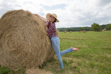 Naklejka na ściany i meble Full length portrait of beautiful countrywoman standing next to hay stack