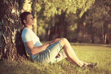 Fototapeta na wymiar Relaxing man sitting under a tree with eyes closed meditating an