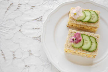 Egg and cucumber afternoon tea sandwiches with edible flowers, copy space lace background