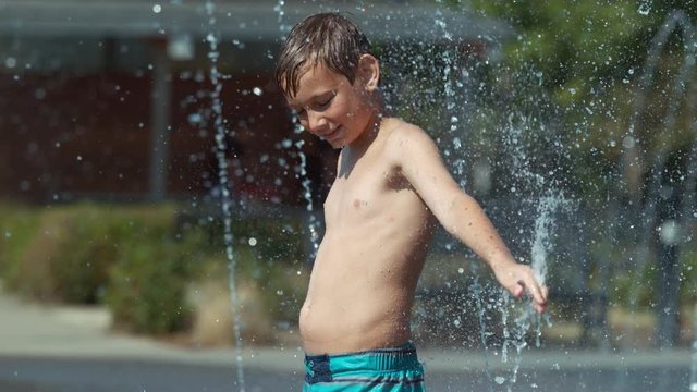 Young boy playing in water fountain, super slow motion