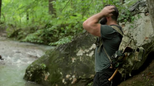 A man hikes down to a flowing creek on a forest trail.