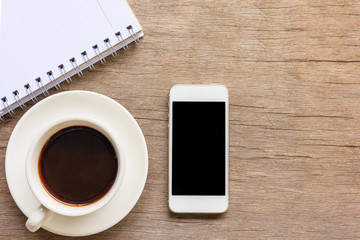 Top view and close up of old wooden desktop with notebook, smartphone and coffee cup.