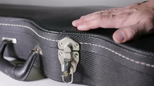 Man's hands open a case and takes a guitar out of a case.