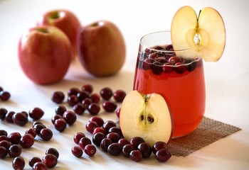 Cranberry Apple Juice in glass surrounded by apples and cranberries. 
