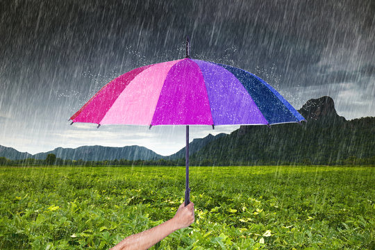 hand holding multicolored umbrella with falling rain at Khao Jee