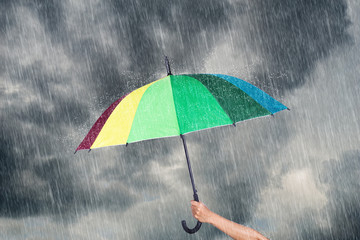 hand holding multicolored umbrella under dark sky with rain