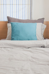 Turquoise and gray pillow on bed with stripe pattern bedding style