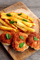 Turkey breast cutlets served with fries on cutting board and on an old wooden background. Cutlets prepared from minced turkey meat and fried in vegetable oil in a frying pan. Closeup. Top view 