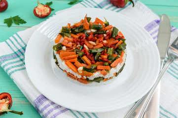 Rice and fried vegetables (asparagus beans, carrots) - vegan diet garnish. Decorated layers of salad on a white plate.