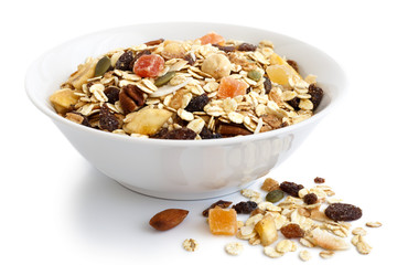 Breakfast bowl of fruit and nut muesli on white. Spilled muesli.