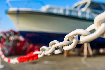 Narrow focus on white and red plastic chain with large blurred motorboat in background.