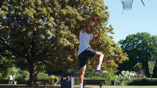 Basketball player slam dunks on an outdoor court, in slow motion